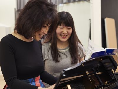 Teacher and student standing at a piano and smiling